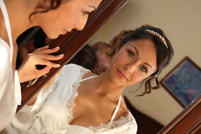 sposa con vestaglia si guarda allo specchio durante la preparazione