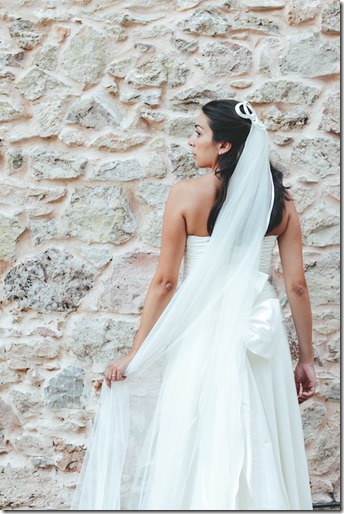 sposa con velo lungo davanti a un muro di pietra